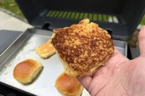 Gegrillte Burgerbuns mit Zucker-Kaneel-Kruste in der Hand, im Hintergrund Smash-Burger-Patties auf dem Grill