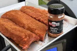 Cadillac Cut Spare Ribs mit BBQPit Pork Rub auf weißem Blech, daneben Gewürzdose mit Würzmischung