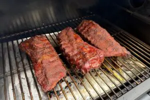 Drei Cadillac-Cut-Spare-Ribs mit Rub-Gewürzmischung auf dem Grillrost eines Smokers während des Garprozesses