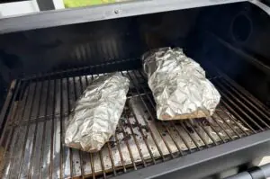 Zwei in Alufolie eingewickelte Cadillac-Cut-Spare-Ribs auf dem Grillrost eines Gasgrillers während des Garprozesses