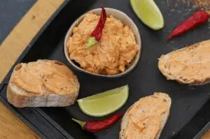 Cajun-Butter auf Toastscheiben verteilt, Schale mit Butter, Limettenspalten und rote Chilischoten auf schwarzem Servierbrett
