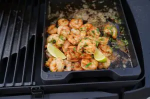 Cajun-Garnelen in würziger Cajun-Butter 11 Cajun-Garnelen in schwarzer Grillpfanne auf dem Grill, gewürzt mit Petersilie, garniert mit Limettenspalten