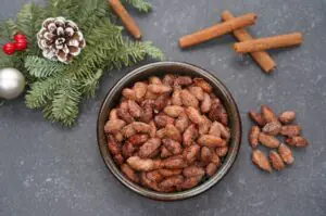 Gebrannte Mandeln aus der Heißluftfritteuse 12 Gebrannte Mandeln in einer Schüssel mit Zimtstangen, Tannenzapfen, Beeren und Kugel als Weihnachtsdeko