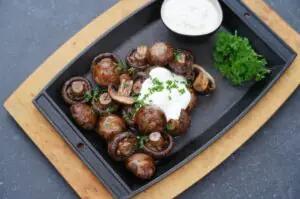 Gegrillte Champignons und Pilze auf schwarzem Tablett mit Sauerrahm und Petersilie, serviert mit Dip
