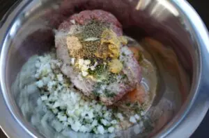 Fleischfrikadellenteig in Schüssel mit gehackten Zwiebeln, Kräutern und Gewürzen vermischt