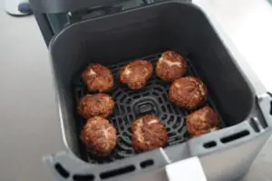 Acht braun gebratene Frikadellen in der Heißluftfritteuse auf dem Gitterrost während der Zubereitung