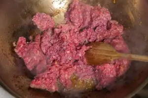 Rohes Rinderhackfleisch wird in einer Wok-Pfanne mit Holzlöffel gerührt und angebraten