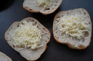 Aufgeschnittene Brötchen mit geriebenem Käse belegt, vorbereitet zum Grillen
