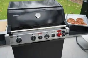 Enders-Gasgrill mit geschlossenem Deckel, daneben Teller mit gegrillten Mettbrötchen mit Käse