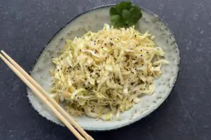 Japanischer Krautsalat in einer Schale, gewürzt mit schwarzem Sesam und Koriander, mit Essstäbchen
