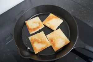 Vier goldbraun gebratene Toastscheiben in schwarzer Gusseisenpfanne, Zubereitungsschritt für Katsu Sando