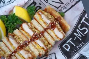 Katsu Sando mit paniertem Schnitzel, Sauce und Sesam zwischen Toastbrot, garniert mit Petersilie und Zitronenscheiben