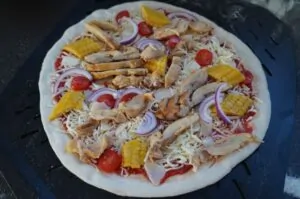 Maishähnchen-Pizza mit Pollo Fino und Mais 8 Maishähnchen-Pizza mit geschreddertem Hähnchenfleisch, Mais, roten Zwiebeln, Tomaten und Käse auf dunklem Grillrost