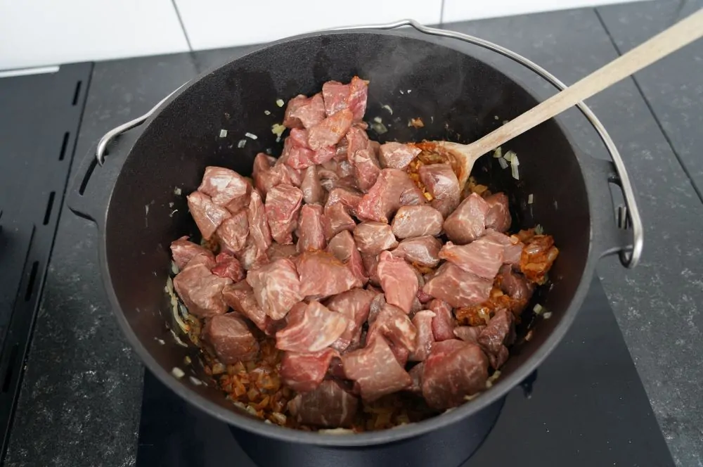 Das Fleisch wird zu den Zwiebeln gegeben