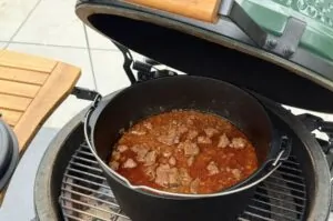 Wiener Saftgulasch mit Fleischstückchen in Soße in einem schwarzen Gusstopf auf dem Grill