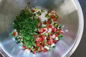 Edelstahlschüssel mit gehackter Petersilie, Tomaten-, Zwiebel- und Paprikawürfeln für Brasilianische Salsa