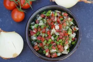 Brasilianische Salsa - Südamerikanische Tomatensalsa 8 Brasilianische Salsa in einer Schüssel mit gewürfelten Tomaten, Zwiebeln, grünen Paprikaschoten und Kräutern. Daneben frische Tomaten und Zwiebelstücke.