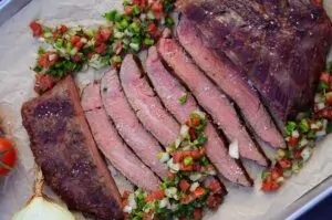 Gegrilltes Flanksteak in dünne Scheiben geschnitten, daneben gehäufte brasilianische Salsa aus Tomaten, Zwiebeln und Koriander