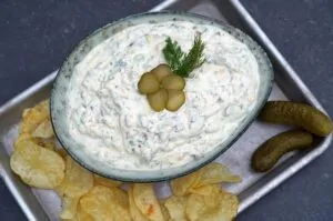 Pickle-Dip in Schale mit Dill-Garnierung und eingelegten Gurkenscheiben, serviert mit Kartoffelchips und Salzgurken