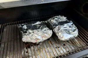 Zwei in Alufolie gewickelte Wildschwein-Ribs auf dem Grillrost beim Garen
