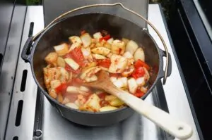 Brauhaus-Gulasch im Dutch Oven auf dem Grill: Kartoffelwürfel und Paprikaschoten werden mit Holzlöffel gerührt