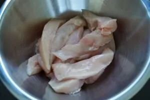 Rohe Hühnerbrustfilets in Streifen geschnitten in einer Edelstahlschüssel zur Vorbereitung von Chicken Fingers