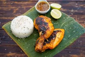 Chicken Inasal - Hähnchen auf philippinische Art 11 Gegrilltes Chicken Inasal mit Brandflecken, serviert auf Bananenblatt mit weißem Reis, Limonenscheiben und Dipping-Sauce
