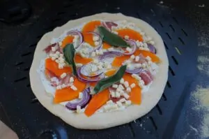 Kürbispizza mit Speck und Salbei 7 Kürbispizza mit Speck, Mozzarella und Salbei auf schwarzem Grillrost, belegt mit Kürbisscheiben, Speckstücken, roten Zwiebeln und frischen Salbeiblättern