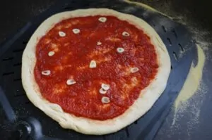 Pizza Marinara - Original-Rezept aus Neapel 8 Pizza Marinara auf dunklem Grillblech mit Tomatensauce und Knoblauchscheiben belegt, vor dem Backen