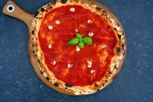 Pizza Marinara - Original-Rezept aus Neapel 10 Pizza Marinara auf Holzbrett: Teig mit dunklen Blasen, rote Tomatensauce, Knoblauchscheiben und frisches Basilikum