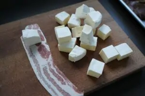 Rindfleischspieße mit Camembert und Bacon 9 Holzbrett mit gewürfeltem Camembert und Baconstreifen als Zutaten für Rindfleischspieße