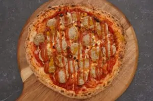 Currywurst-Pizza auf Holzbrett: Tomatensauce, Mozzarella, Currywurstscheiben und rote Paprika mit Curryhonig-Drizzle
