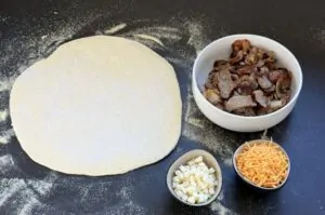 Ausgerollter Pizzateig mit Zutaten für Döner Bomb: Schüssel mit Dönerfleisch, gehackte Zwiebeln und geriebener Käse auf mehliger Arbeitsfläche