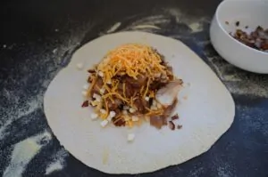 Tortilla mit Döner-Füllung aus Fleisch, gehackten Zwiebeln, Käsestücken und knusprigen Speckstücken