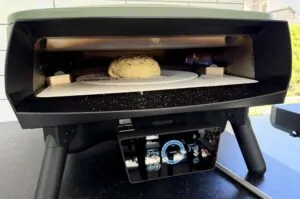 Döner-Bomb-Pizza im Pizzaofen auf kreisförmigem Stein, Flammen im Hintergrund, digitales Thermometer zeigt 318°C