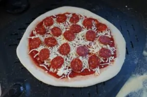 Ungegarte Pepperoni-Pizza auf Grillplatte: Pizzaboden mit Tomatensoße, geschreddertem Käse und Peperoni-Scheiben belegt