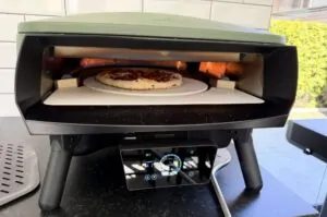 Pizza Peperoni mit Peperoni-Belag in Pizzaofen auf Schamottstein, Flammen sichtbar, während des Backens