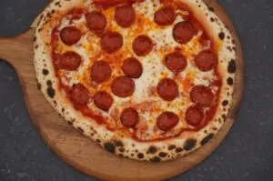 Pepperoni-Pizza auf Holzbrett mit knuspriger Kruste, Tomatensoße, geschmolzenem Käse und zahlreichen Peperoni-Scheiben
