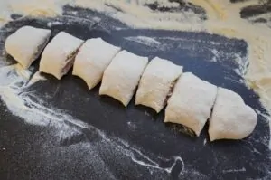 Sechs gefüllte Pizzabrötchen mit Schinken und Käse auf mehlbestäubter dunkler Arbeitsfläche, vor dem Backen.