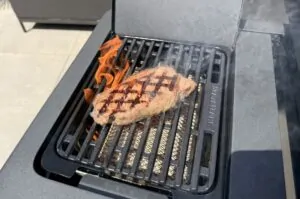Rumpsteak mit Grillmarkierungen auf heißem Gasgrill mit Flammen, Seitenschaufel sichtbar
