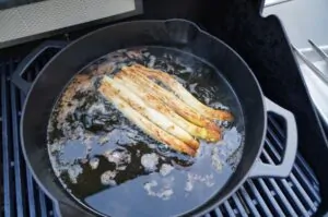 Gebratener weißer Spargel in schwarzer Gusseisen-Pfanne auf dem Grill, mit Bratspuren