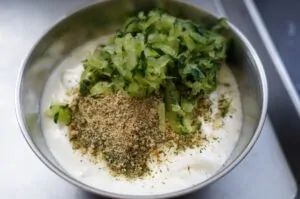 Schüssel mit Tzatziki-Sauce, frischen Gurkenstücken und Kräutern, oben mit Gewürzmischung bestreut