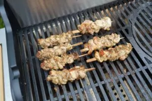 Gyros-Hähnchenspieße auf Holzspießen grillen auf schwarzem Grillrost, zeigen gebräunte Oberflächen und Gewürzkruste