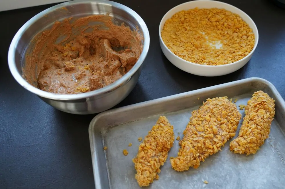 Die Hähnchenstreifen werden mit zerbröselten Cornflakes paniert